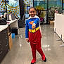 child, superhero_costume, supergirl, blue_top, red_pants, white_cape, smiling, posing, office, glass_wall, polka_dots, chair, desk, box, floor, indoor, modern, young_girl, happy, costume