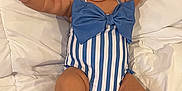 Malia is registered to the contest to win money with this photo: baby, child, infant, sunglasses, blue_bow, striped_swimsuit, headband, white_quilt, lying_down, arms_up, cute, fashion, accessories, portrait, indoor, relaxed, smiling, chubby, person, baby_fashion