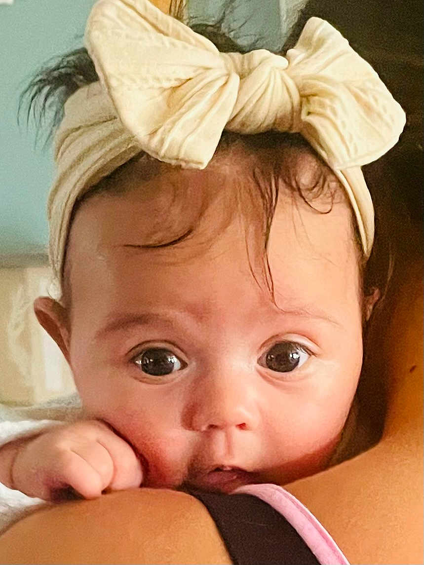 Malia joined the competition — help win amazing prizes! baby, close_up, headband, bow, face, child, cute, skin, eyes, person, infant, hand, portrait, expression, soft_light, human, shoulder, indoor, adorable, young