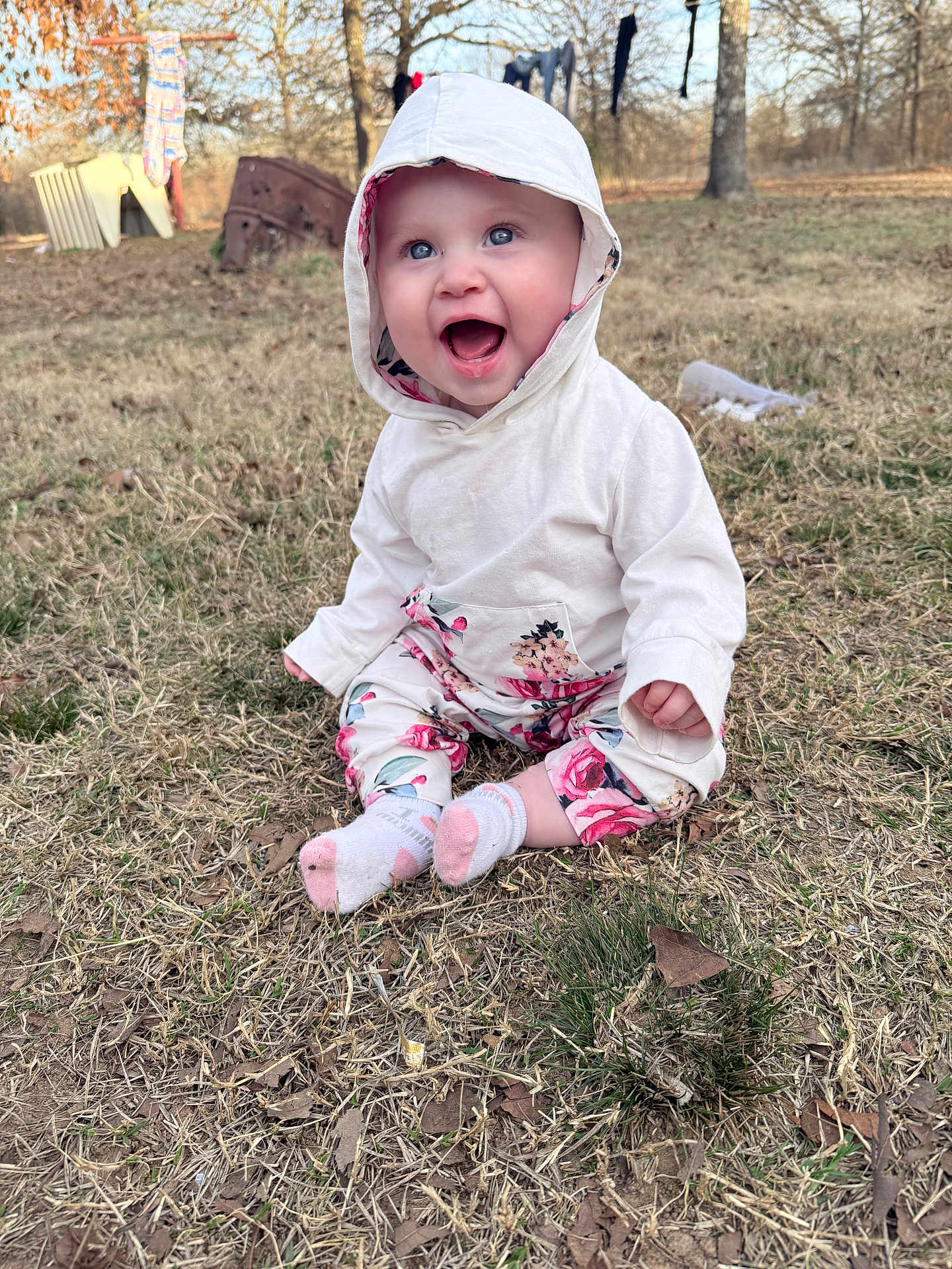 Ryleigh Graffam joined the competition — help win amazing prizes! baby, child, hoodie, floral_pants, grass, outdoor, smile, happy, sitting, nature, trees, leaf_litter, cute, infant, casual_clothing, bright_eyes, playful, seasonal, joyful, portrait