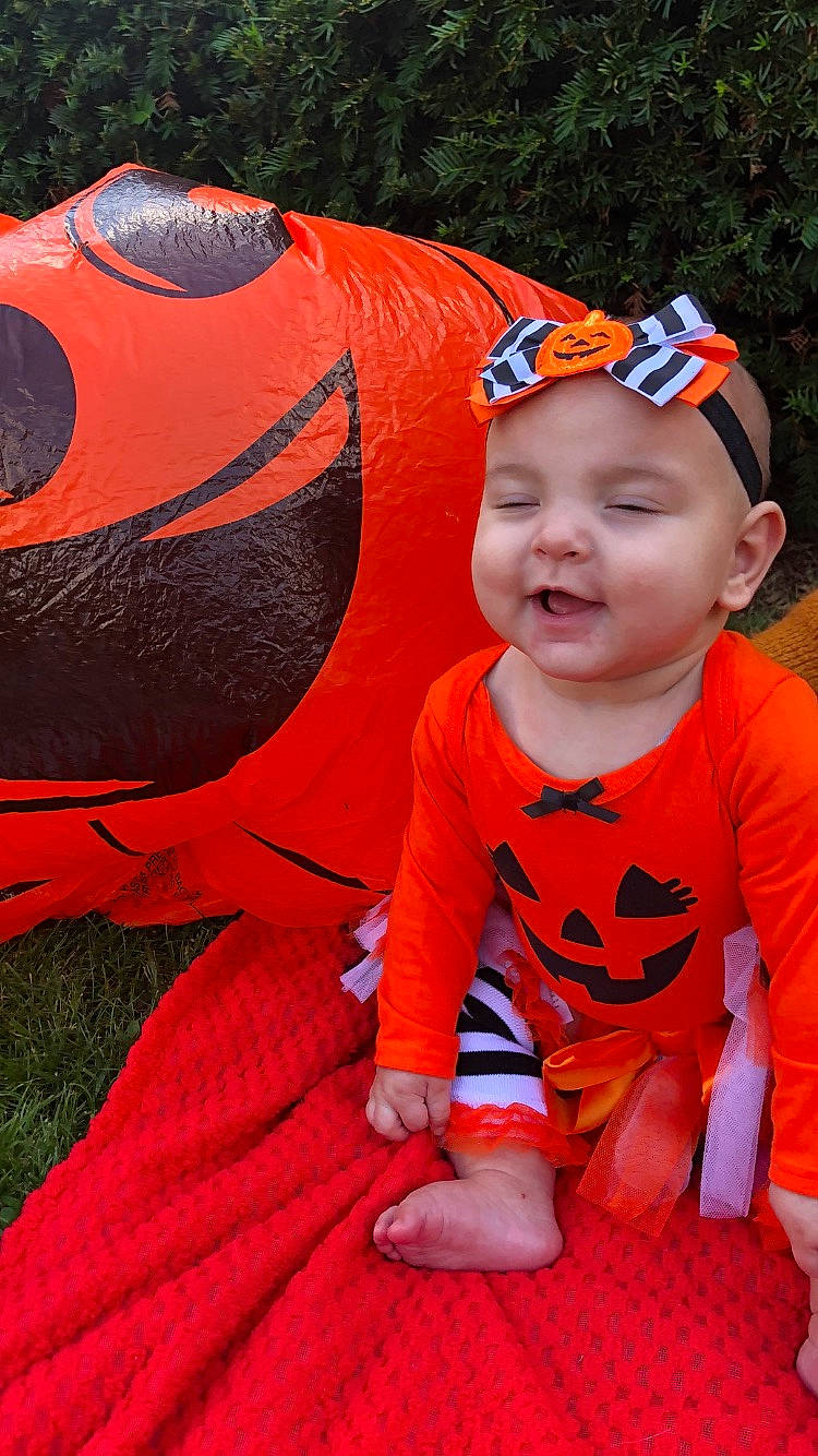 Jocelyn is registered to the contest to win money with this photo: baby, baby_toddler_clothing, cap, child, fun, goggles, grass, happy, headwear, leisure, mouth, orange, person, personal_protective_equipment, pink, plant, recreation, red, sitting, sunglasses