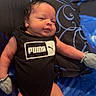 Lionel is registered to the contest to win money with this photo: baby, bed, black, black_clothing, blanket, blue, child, face, hands, indoors, infant, legs, lying_down, mittens, newborn, onesie, photography, portrait, puma_logo, skeptical_expression