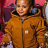 child, smiling, braids, beads, brown_jacket, purse, gift_box, golden_furniture, portrait, indoor, cute, fashion, accessory, happy, young_child, person, holiday, decor, cozy, cute_expression