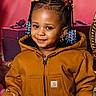 child, toddler, braids, beads, jacket, brown_jacket, smile, purse, sparkly_purse, gift_boxes, indoor, portrait, cute, fashion, earrings, happy, person, holiday, decor, furniture