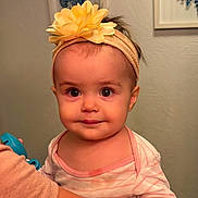 Chloe is registered to the contest to win money with this photo: baby, child, headband, flower, yellow, face, eyes, arm, clothing, striped, person, portrait, indoor, skin, hand, looking, cute, infant, wall_art, decor