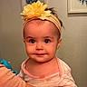 baby, child, headband, flower, yellow, face, eyes, arm, clothing, striped, person, portrait, indoor, skin, hand, looking, cute, infant, wall_art, decor