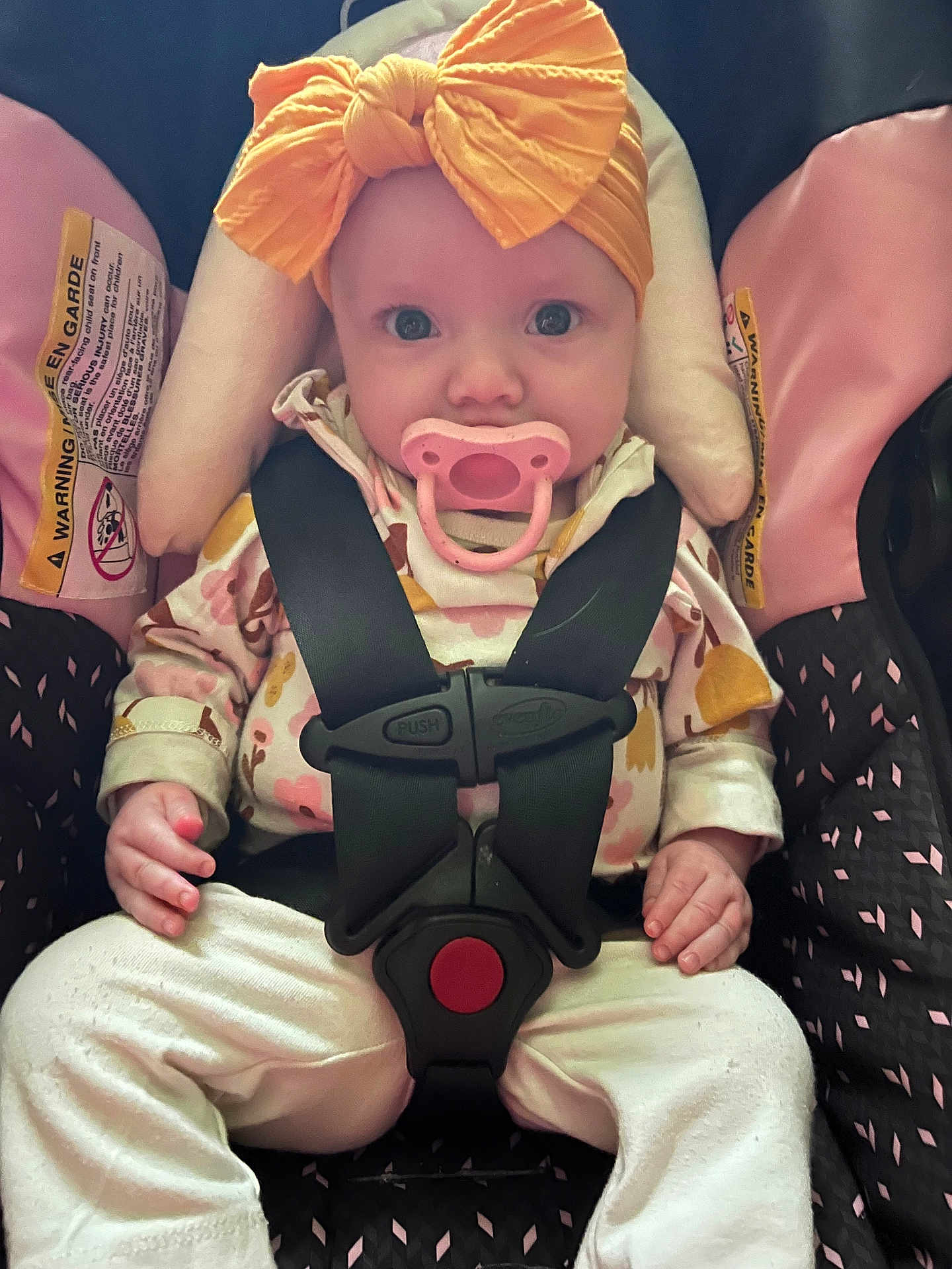 Drew joined the competition — help win amazing prizes! baby, car_seat, pacifier, yellow_bow, child, infant, seatbelt, clothing, pink, white_pants, cute, face, hands, sitting, portrait, indoor, child_safety, straps, headwear, curious