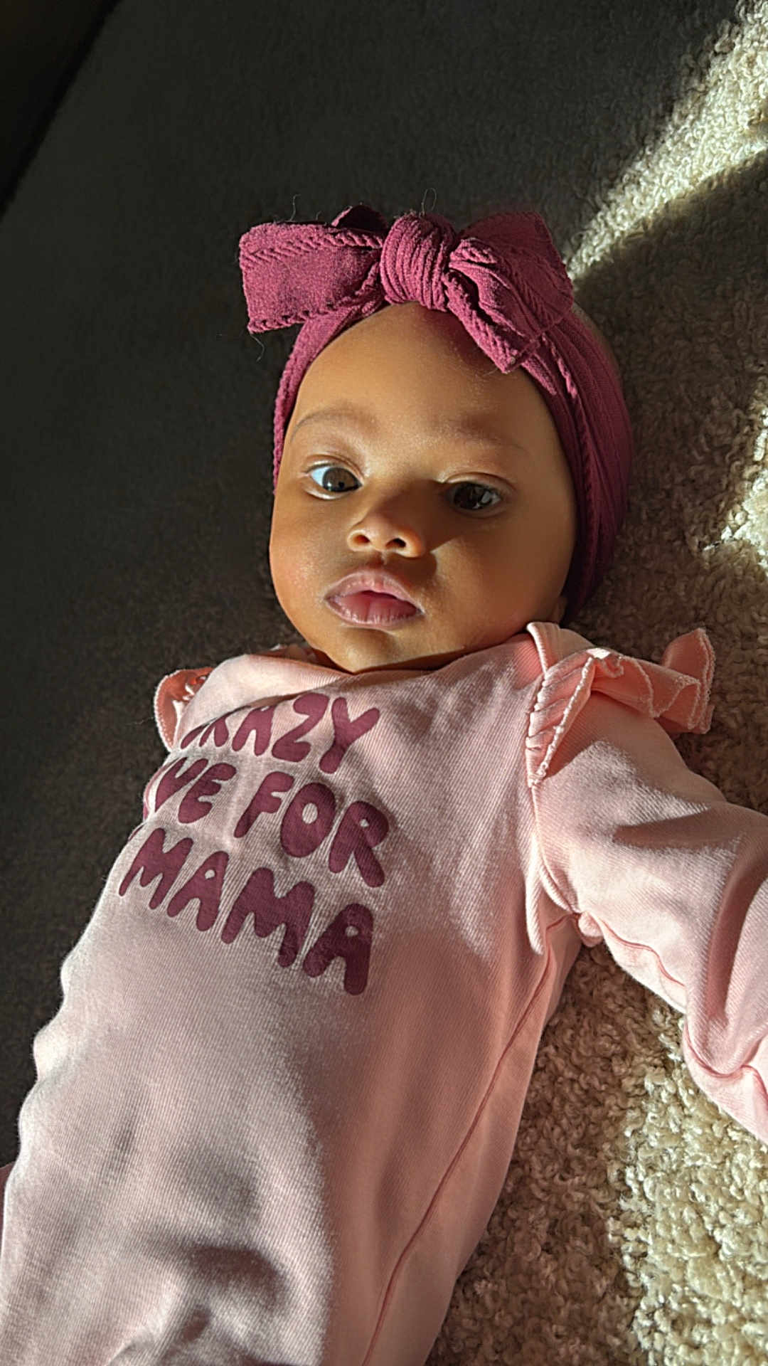 Kylie joined the competition — help win amazing prizes! baby, infant, child, headband, pink_clothing, onesie, text_on_clothing, carpet, sunlight, portrait, face, cute, indoor, soft_light, lying_down, chubby_cheeks, expression, young_child, apparel, human