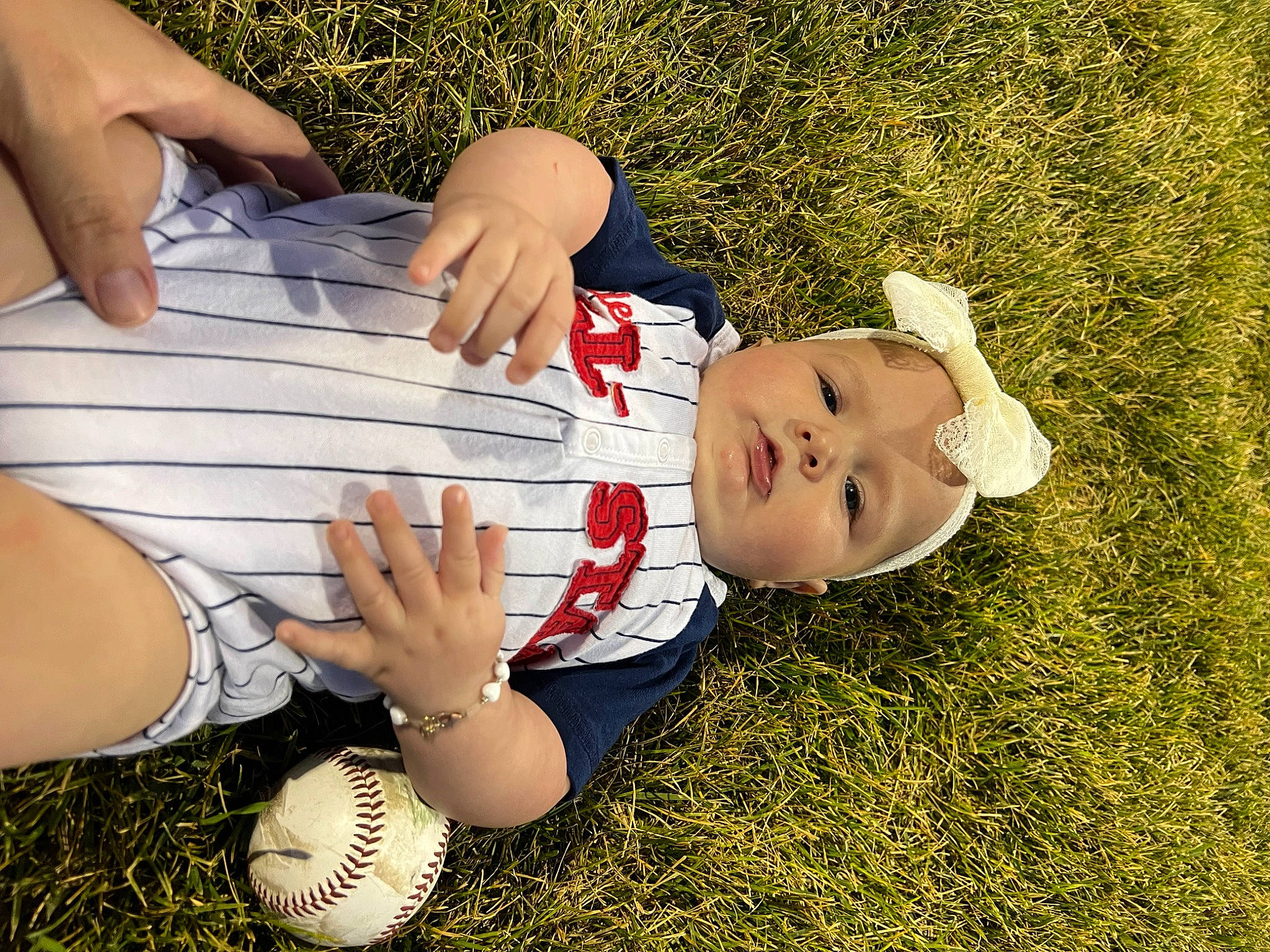 Meadow is registered to the contest to win money with this photo: arm, baby, baby_toddler_clothing, finger, gesture, grass, hand, happy, hat, human_body, human_leg, leg, leisure, people_in_nature, person, plant, smile, thigh, thumb, toddler