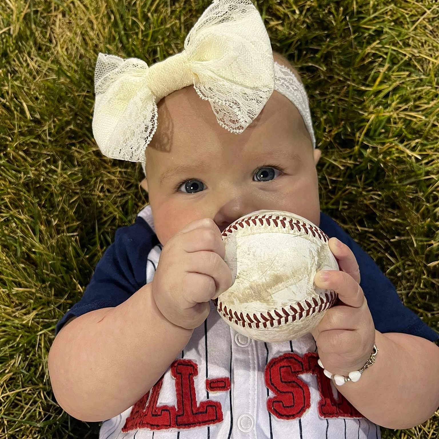 Meadow is registered to the contest to win money with this photo: baby_toddler_clothing, ball, baseball_glove, cap, clothing, eye, gesture, glove, grass, hand, happy, hat, head, headgear, nose, people_in_nature, personal_protective_equipment, plant, toddler, white