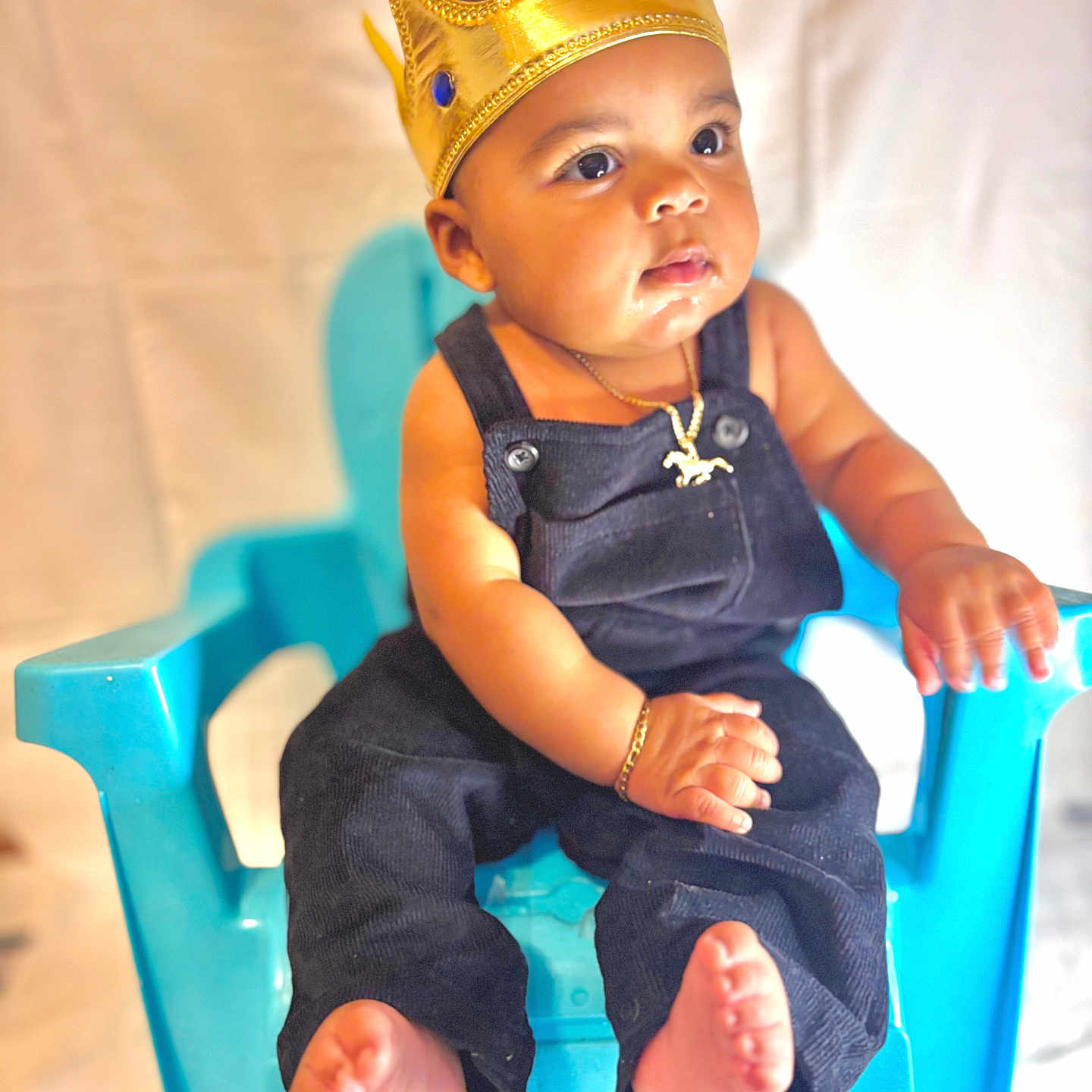 Kylian is registered to the contest to win money with this photo: baby, baby_clothes, blue_chair, bracelet, child, crown, cute, expression, foot, golden_crown, hand, indoor, infant, jewelry, necklace, overalls, person, portrait, sitting, skin