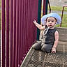 toddler, child, hat, playground, metal_platform, pink_bars, outdoor, grass, serious_expression, sitting, daylight, person, clothing, play_area, summer, young_child, cute, kid, mesh_surface, sunhat