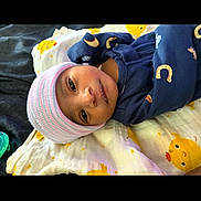 Kmazi Edwards is registered to the contest to win money with this photo: baby, infant, child, portrait, lying_down, blanket, knit_hat, winter_clothing, navy_outfit, striped_hat, duck_pattern, bed, indoor, face, eyes, looking_at_camera, calm, cute, textile, photography