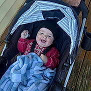 Dakota joined the competition — help win amazing prizes! baby, infant, child, stroller, smiling, happy, pacifier, blanket, hat, red_sweater, portrait, outdoor, wooden_deck, canopy, caregiver, adult, hands, tattoo, cozy, family