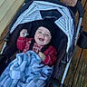 baby, infant, child, stroller, smiling, happy, pacifier, blanket, hat, red_sweater, portrait, outdoor, wooden_deck, canopy, caregiver, adult, hands, tattoo, cozy, family
