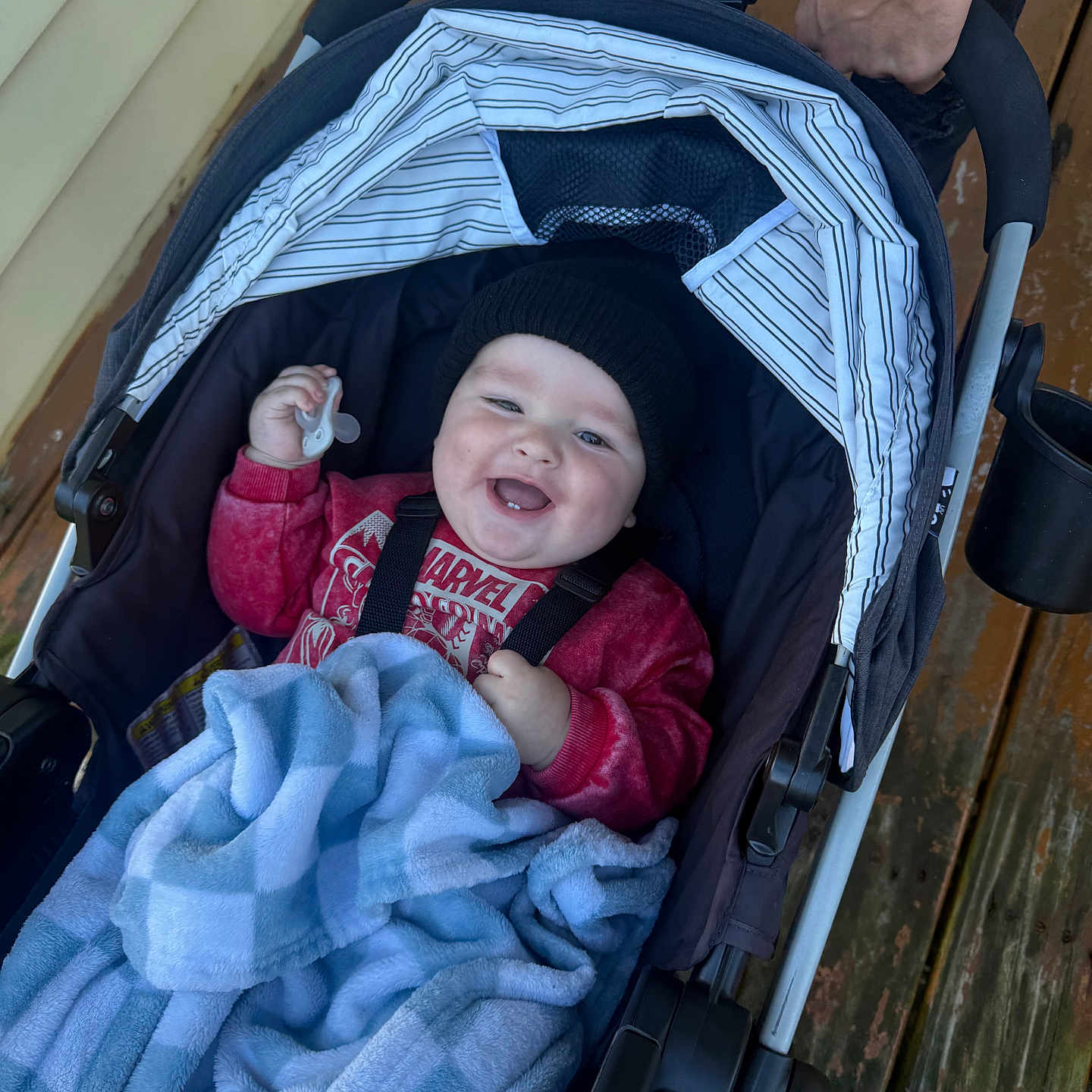 Dakota joined the competition — help win amazing prizes! baby, infant, child, stroller, smiling, happy, pacifier, blanket, hat, red_sweater, portrait, outdoor, wooden_deck, canopy, caregiver, adult, hands, tattoo, cozy, family