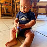 baby, child, infant, sitting, indoor, kitchen, wooden_chairs, tile_floor, portrait, face, looking_down, short_hair, navy_shirt, clothing, barefoot, toy, colorful_object, warm_lighting, home, cute