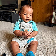Aslan joined the competition — help win amazing prizes! baby, child, infant, sitting, carpet, indoors, living_room, overalls, blue_shirt, blue_socks, hands, face, portrait, looking_down, wooden_door, television, furniture, home, smiling, photography
