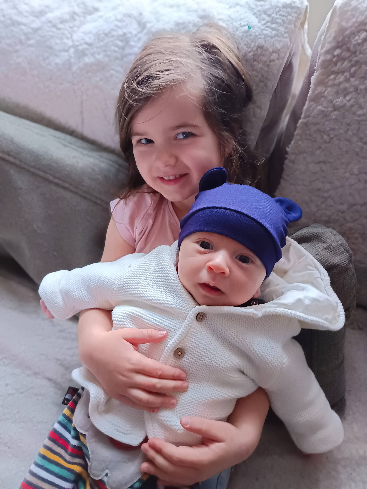 Sacha a rejoint le concours — aidez-le/la à gagner de superbes lots ! baby, blanket, child, clothing, couch, cozy, cute, face, family, happy, hat, holding, indoors, infant, person, portrait, sibling, smile, sweater, warm