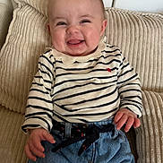 Gabrielle a rejoint le concours — aidez-le/la à gagner de superbes lots ! baby, smiling, striped_shirt, denim, pants, cushion, beige, happy, sitting, child, face, person, indoor, clothing, cute, portrait, young_child, joyful, hand, cozy