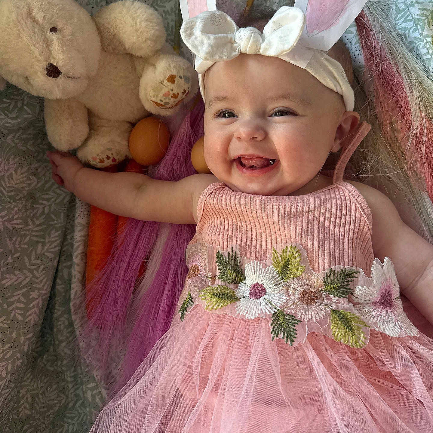 Gabrielle participe au concours pour gagner de l'argent avec cette photo : baby, child, smiling, pink_dress, bunny_ears, headband, plush_toy, stuffed_animal, toy, blanket, happy, cute, portrait, infant, flower_embroidery, fabric, lying_down, indoor, colorful, playful