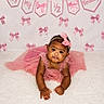 baby, child, infant, pink_dress, headband, bow, carpet, celebration, birthday, half_birthday, banner, decorations, cute, portrait, smiling, happy, lying_down, indoors, soft_texture, curious