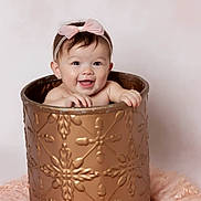 Isabella is registered to the contest to win money with this photo: baby, child, smile, pink_bow, headband, bucket, golden_bucket, happy, portrait, cute, infant, hands, face, studio_photo, soft_background, fluffy, decorative_bucket, toddler, indoors, adorable