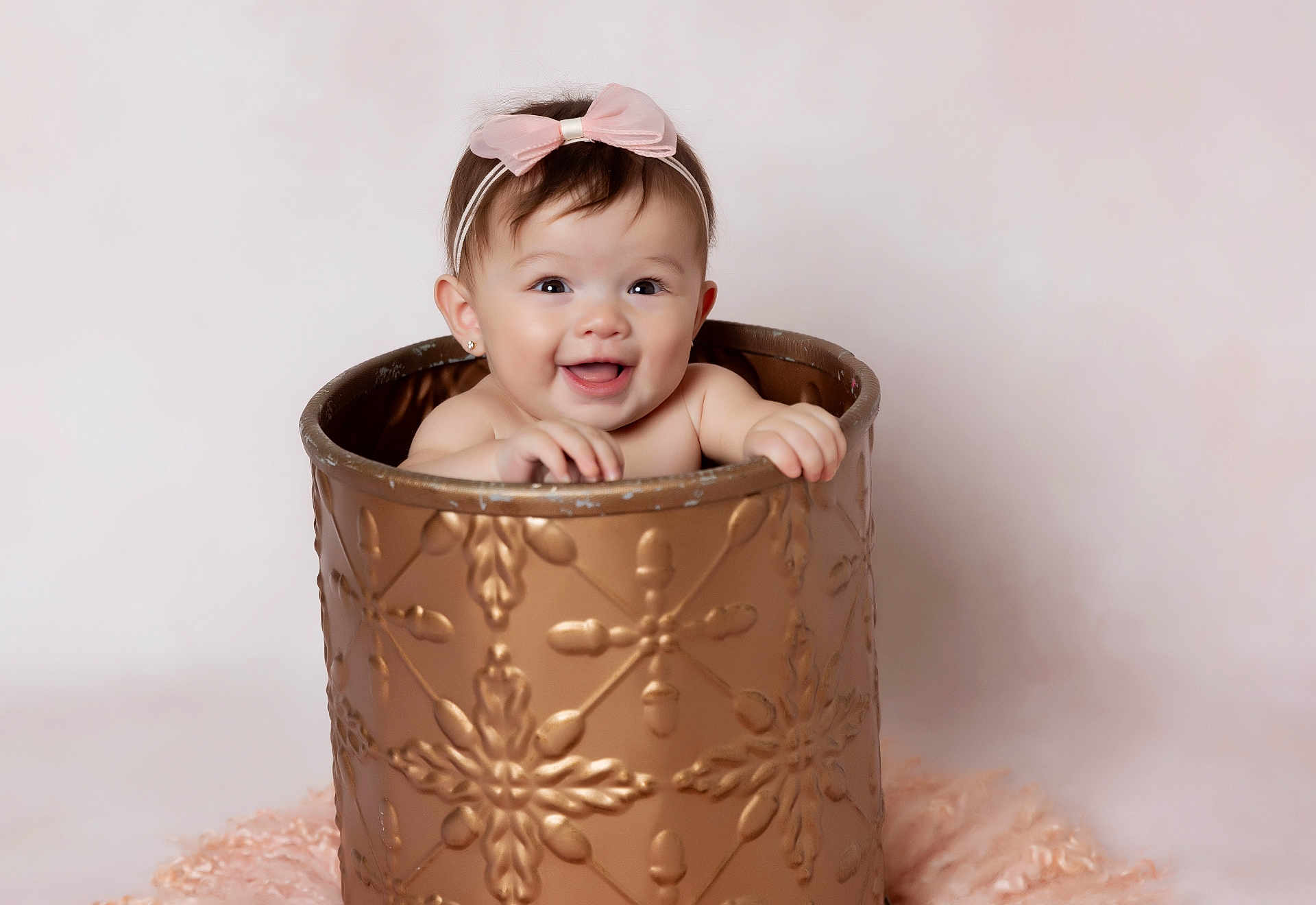 Isabella is registered to the contest to win money with this photo: baby, child, smile, pink_bow, headband, bucket, golden_bucket, happy, portrait, cute, infant, hands, face, studio_photo, soft_background, fluffy, decorative_bucket, toddler, indoors, adorable