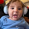 baby, child, headphones, blue_shirt, nike_logo, airplane_interior, seat, person, portrait, smiling, cute, face, hair, clothing, toddler, travel, happy, infant, closeup, young