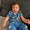 toddler, child, smiling, curly_hair, blue_pajamas, donald_duck, sitting, couch, gray_cushion, happy, indoor, portrait, cute, playful, clothing, person, young_child, relaxed, home, baby