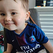 Marlon participe au concours pour gagner de l'argent avec cette photo : toddler, child, smiling, face, blue_jersey, paris_saint_germain, sportswear, indoor, chair, home_office, cabinet, drawer, light, person, cute, happy, short_hair, pants, pattern, casual