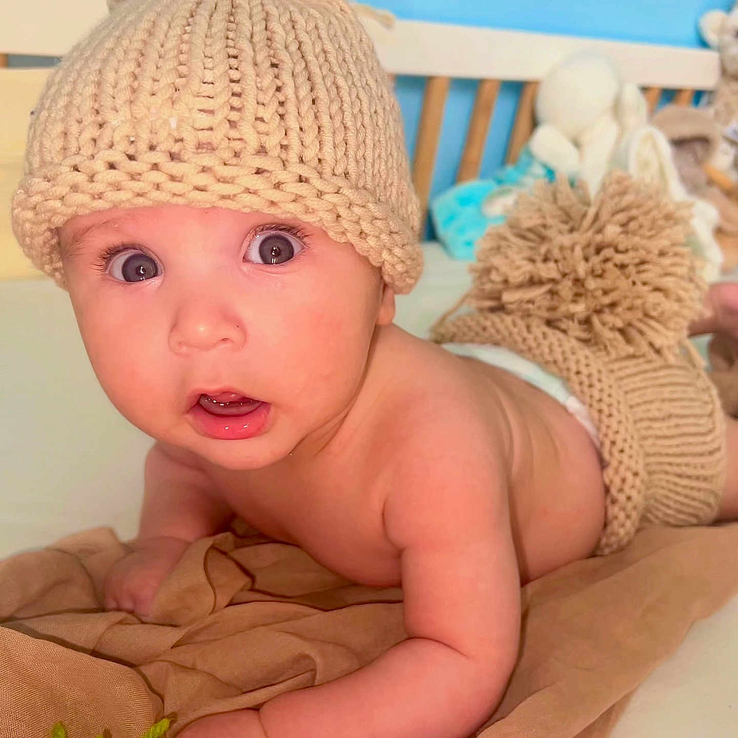 Liandro a rejoint le concours — aidez-le/la à gagner de superbes lots ! baby, blanket, child, cozy, crib, cute, headwear, indoor, infant, knit_diaper_cover, knit_hat, nursery, person, plush_toys, portrait, skin, soft_lighting, surprised_expression, tummy_time, wide_eyes