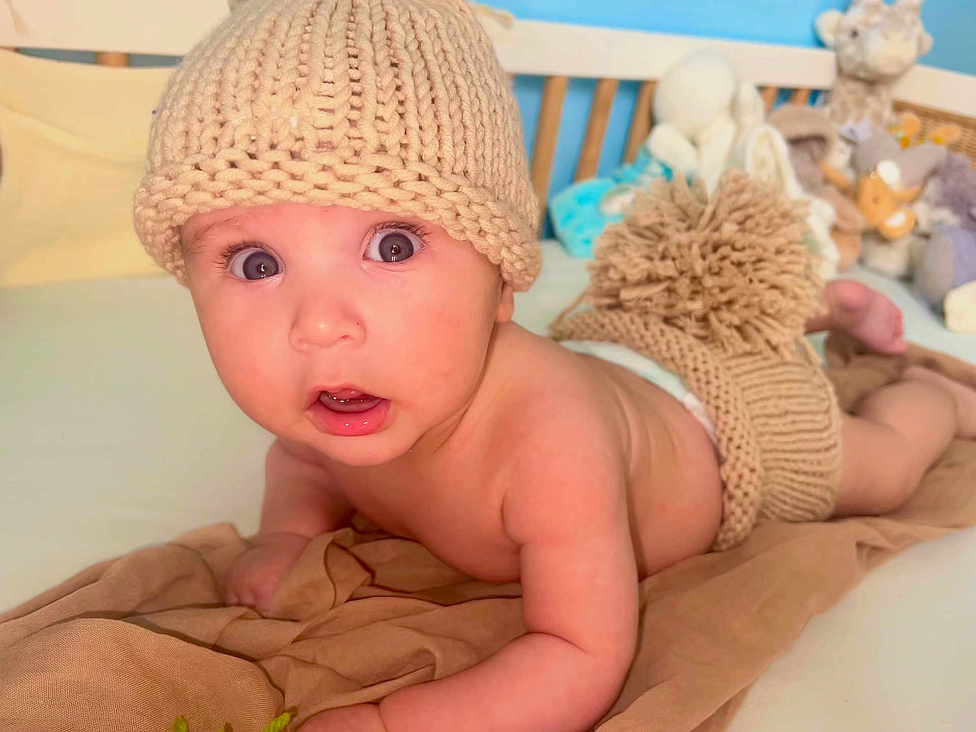 Liandro a rejoint le concours — aidez-le/la à gagner de superbes lots ! baby, blanket, child, cozy, crib, cute, headwear, indoor, infant, knit_diaper_cover, knit_hat, nursery, person, plush_toys, portrait, skin, soft_lighting, surprised_expression, tummy_time, wide_eyes