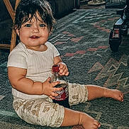 Jesse is registered to the contest to win money with this photo: baby, child, indoor, sitting, carpet, bottle, drink, dr_pepper, clothing, patterned_pants, barefoot, wet_hair, blue_eyes, tongue_out, cute, floor, furniture, slippers, toy_vehicle, happy
