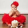 accessory, baby, celebration, child, cup, cute, festive, floor, food, headwear, holiday, holiday_season, indoor, marshmallows, portrait, red_headband, sitting, smiling, toddler, tutu