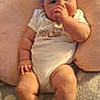 baby, carpet, chubby_arms, chubby_legs, comfort, cozy, curious_expression, cushion, face, head, indoors, infant, person, pillow, seated, skin, socks, soft_texture, thumb_sucking, white_onesie