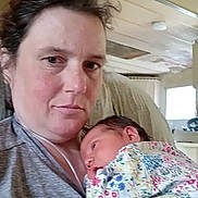 Scarlett is registered to the contest to win money with this photo: woman, baby, newborn, holding, indoor, selfie, person, face, clothing, floral_pattern, resting, casual, expression, hair, skin, room, furniture, window, watermark, technology