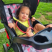 Madeline is registered to the contest to win money with this photo: baby, black_strap, child, face, foot, grass, hand, happy, outdoor, park, person, pink_pattern, playground, seat, smile, stroller, toddler, toy, wheel, yellow_clothing