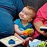 adult, blocks, blue_shirt, child, couch, face, family, footwear, furniture, hand, indoor, legs, person, pink_shirt, playtime, sitting, smile, sneakers, toddler, toy