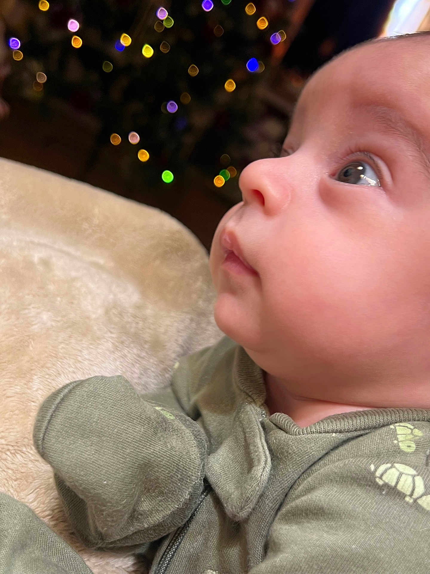 Luca joined the competition — help win amazing prizes! baby, infant, close_up, profile, face, child, green_clothing, turtle_print, blanket, soft_texture, bokeh, colorful_lights, indoors, cute, small_hands, young_child, cozy, warm, looking_up, portrait