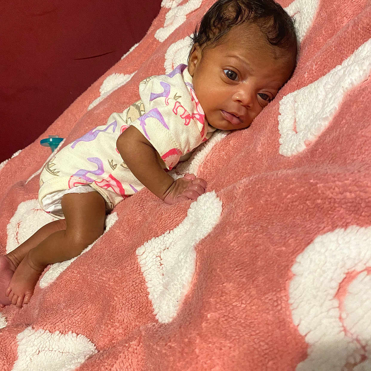 Kyari is registered to the contest to win money with this photo: baby, blanket, child, curious, cute, dinosaur_pattern, face, foot, hand, indoors, infant, lying_down, newborn, onesie, pink, resting, skin, sleepwear, soft_texture, white