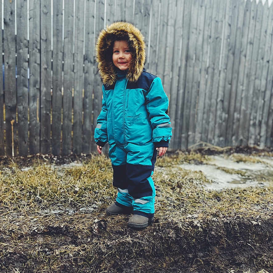 Willow is registered to the contest to win money with this photo: boy, child, clothing, coat, face, fence, glove, hat, head, hood, jacket, longsleeve, male, outdoors, pants, person, photography, portrait, sleeve, soil
