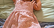 Mylah joined the competition — help win amazing prizes! arms_up, baby, blanket, bow, child, comfortable, cute, fabric, happy, headband, indoors, infant, lying_down, person, pink_dress, portrait, smiling, soft_texture, striped_bedding, young_child