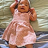 arms_up, baby, blanket, bow, child, comfortable, cute, fabric, happy, headband, indoors, infant, lying_down, person, pink_dress, portrait, smiling, soft_texture, striped_bedding, young_child