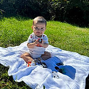 Leo joined the competition — help win amazing prizes! baby, toy_car, blanket, grass, outdoor, greenery, sunlight, smile, child, nature, play, sitting, happy, shorts, shirt, footwear, shadow, leaf, daytime, toy