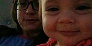 Amara joined the competition — help win amazing prizes! baby, infant, adult, glasses, selfie, smile, face, close_up, indoor, dim_light, grainy, portrait, parent_and_child, bedroom, headboard, shirt, red_dress, happy, candid, person