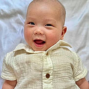 Elias is registered to the contest to win money with this photo: baby, infant, smile, happy, face, child, person, clothing, buttoned_shirt, short_sleeves, lying_down, white_blanket, skin, head, eyes, mouth, indoors, cute, young, portrait