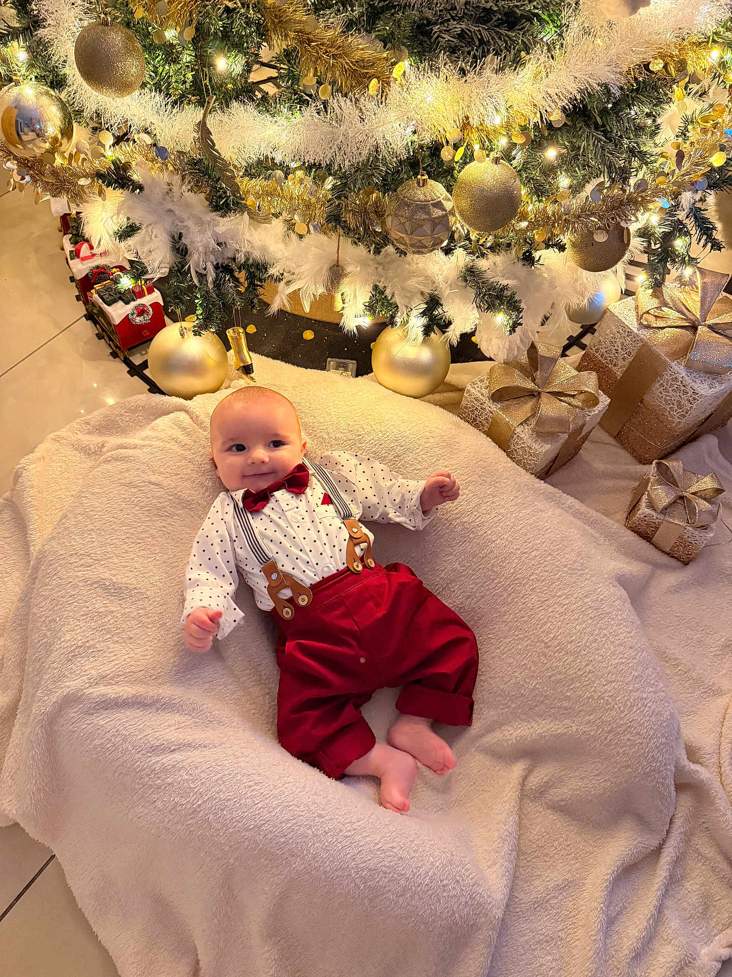 Gabriel participe au concours pour gagner de l'argent avec cette photo : baby, christmas_tree, ornaments, golden_balls, presents, blanket, holiday, festive_clothing, bow_tie, suspenders, smiling, indoors, decorations, lights, floor_tiles, wrapped_gifts, holiday_season, cute, infant, celebration
