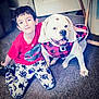 boy, child, dog, bulldog, pet, carpet, indoor, clothing, red_shirt, patterned_pants, smile, happy, friendship, animal, canine, young, sitting, cozy, cute, portrait