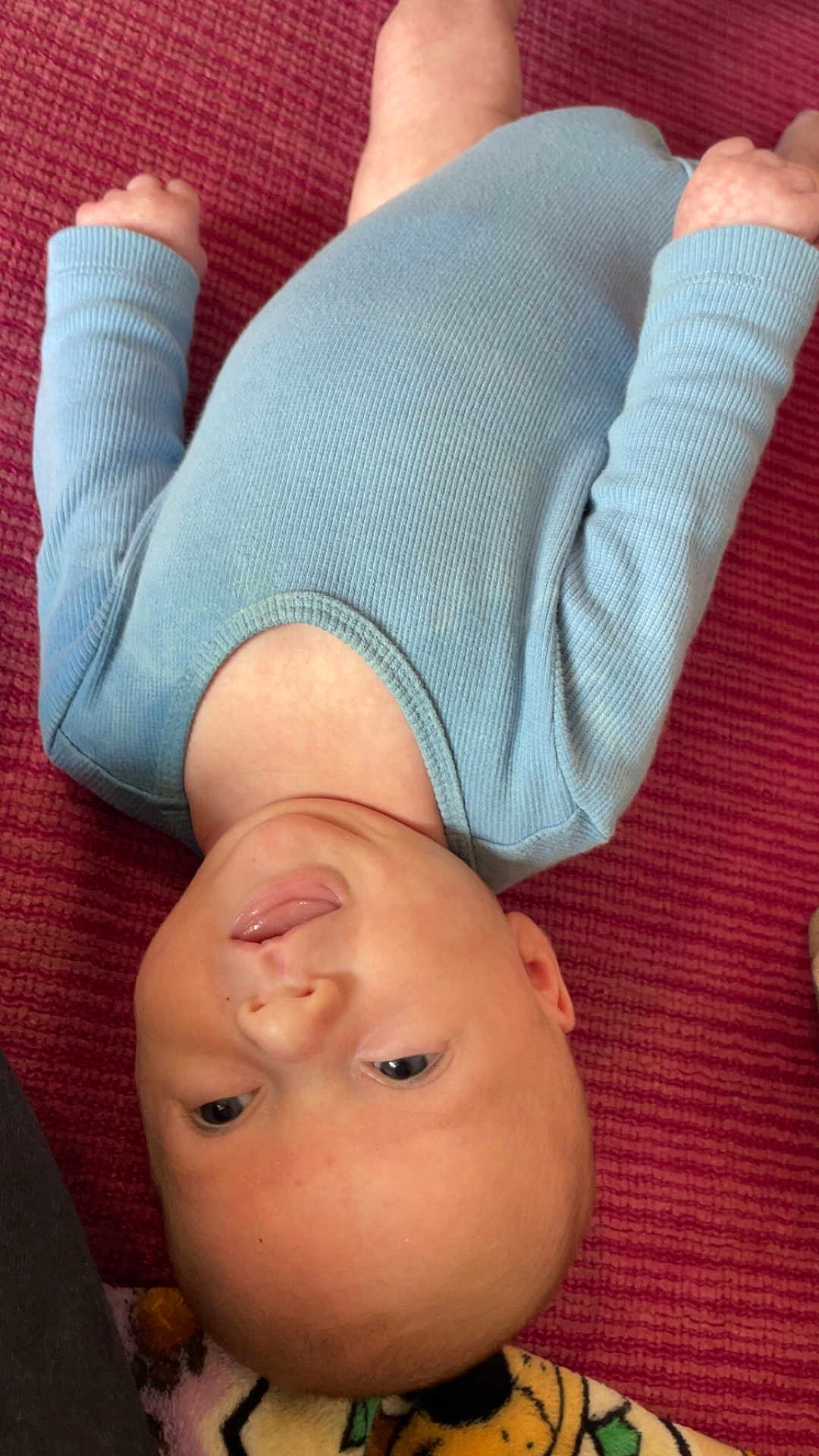 Khaison joined the competition — help win amazing prizes! baby, infant, child, lying_down, blue_clothing, tongue_out, playful, cute, skin, head, face, eyes, hands, onesie, textured_background, red_background, soft_light, indoors, human, portrait